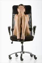Naked Caucasian woman wearing high heels covering face in chair