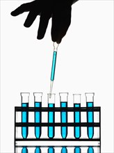 Hand holding pipette dripping blue liquid into test tubes
