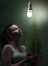Caucasian woman holding potted plant under cfl lightbulb