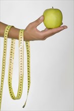 Hand of Caucasian woman holding green apple and measuring tape