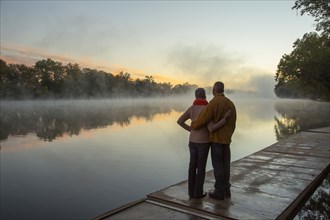 Older couple hugging at foggy river at sunrise