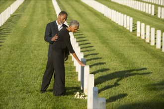 Black couple touching gravestone at military cemetery