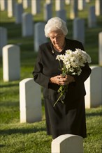 Caucasian widow holding bouquet at cemetery gravestone