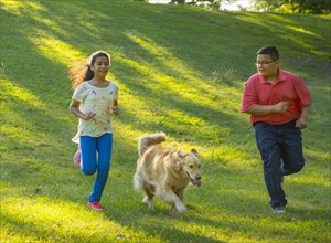 Hispanic brother and sister running with dog on hill