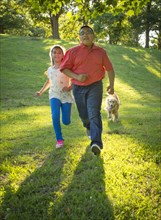 Hispanic brother and sister running with dog on hill
