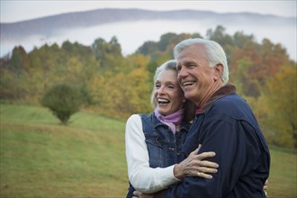 Older Caucasian couple hugging in field