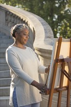 Black woman painting on canvas near stone staircase