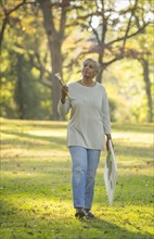 Pensive Black woman carrying paintbrushes and canvas in park