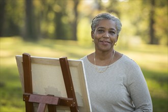 Portrait of Black woman painting on canvas in park