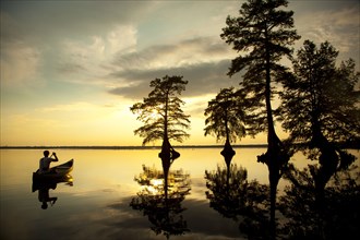 Reflection of Caucasian boy in canoe near trees in river