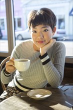 Serious Asian teenage girl drinking coffee in coffee shop