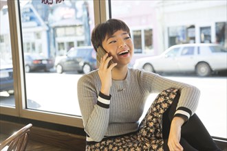 Asian teenage girl talking on cell phone on window sill