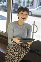 Asian teenage girl using digital tablet on window sill