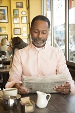 Mixed Race man reading newspaper in coffee shop