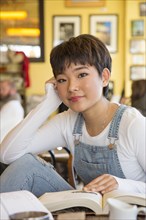 Asian teenage girl reading book in coffee shop