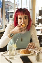 Caucasian woman eating croissant in restaurant