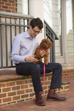 Caucasian man holding dog and texting on cell phone