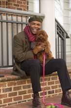Portrait of African American man sitting on stoop holding dog