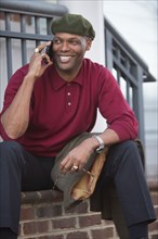 African American man sitting on stoop talking on cell phone