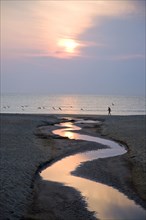 Man walking on beach near water channel at sunset