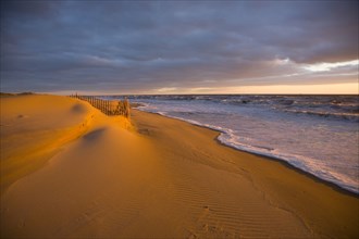 Ocean waves near sand dunes at sunset
