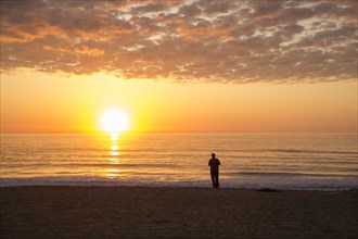Silhouette of man standing on ocean beach at sunset
