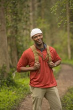 African American man standing on path in forest carrying backpack