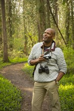 African American man standing on path in forest holding camera