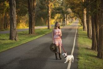 Caucasian woman holding a cowboy hat walking dog