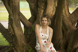 Caucasian teenage girl sitting on tree root holding flute
