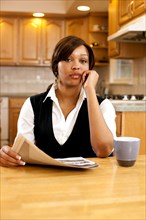 Serious African woman with paperwork and coffee in kitchen