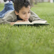 Boy reading book while lying on lawn