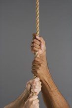 Close up of four hands hanging on rope