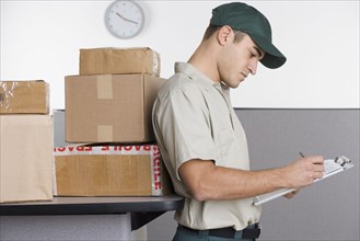 Profile of delivery man writing in clipboard with stack of boxes behind him