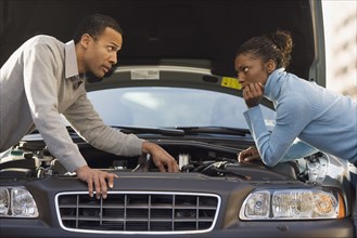 Mechanic explaining to woman while leaning over car