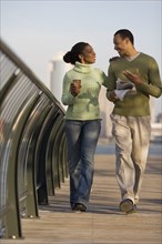 Couple walking across bridge with city behind them