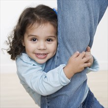 Portrait of young girl hugging leg of mother