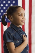 Young girl holding her hand across her heart with American flag in background