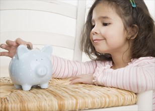 Young Hispanic girl putting coin in piggy bank