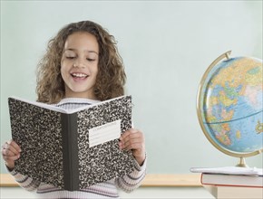 Young girl reading from notebook in classroom