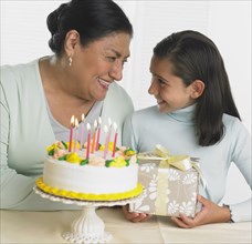 Hispanic grandmother and granddaughter with birthday cake and gift