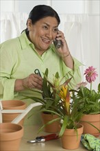 Senior Hispanic woman gardening indoors and using telephone