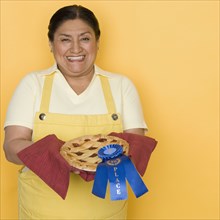 Senior Hispanic woman holding pie with first place ribbon