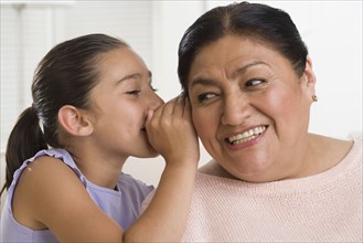 Hispanic girl whispering in grandmother's ear