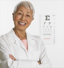 Senior Asian female doctor with eye chart in background