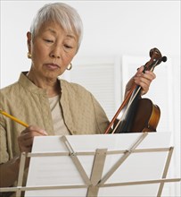 Senior Asian woman with violin and sheet music