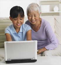 Asian grandmother and granddaughter using laptop on sofa