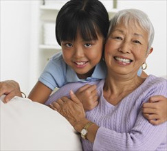 Asian grandmother and granddaughter hugging and on sofa