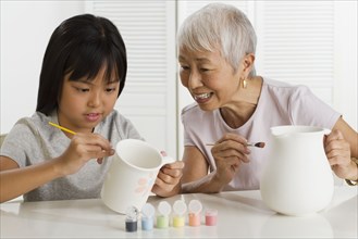 Asian grandmother and granddaughter painting pottery