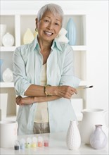 Senior Asian woman smiling with pottery and paints